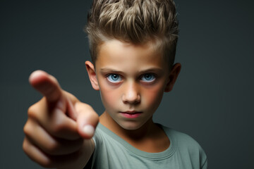 Little boy with a serious expression on his face pointing finger at someone isolated on gray background with copy space