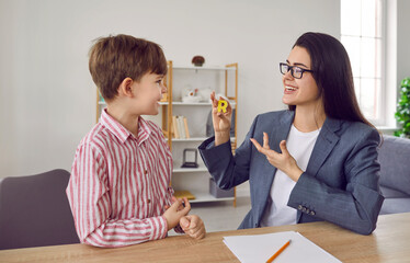 Speech therapist and boy patient training articulation in office. Young woman teacher showing...