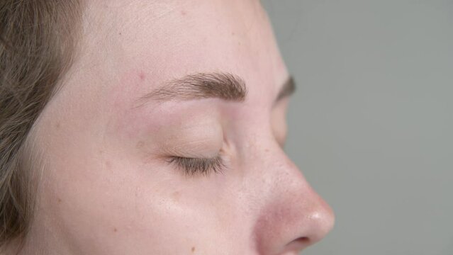 Beautician rinses cleanser from client's eyebrows. Preparing eyebrows for permanent coloring. Close-up of the face of a young Caucasian woman and the hands of a cosmetologist.