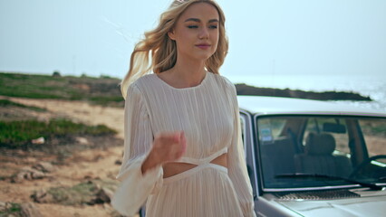 Blonde girl walking seashore with retro car on backdrop closeup. Woman strolling