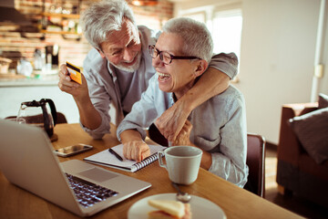 Fototapeta na wymiar Happy senior couple using credit card on laptop at home