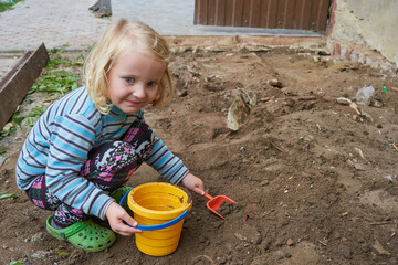 little girl is playing on the construction site, a child is playing in the yard with a bucket and a shovel