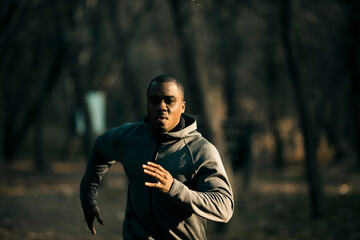 Focused runner in a hoodie jogging through a forested park at dusk