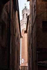 Tower of the Palazzo Pubblico at the Piazza del Campo in downtown Siena, seen from a narrow alleyway