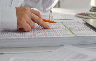 Man works with paper balance sheets. Accountant reviewing enterprise profit, holding pencil in hand and checking columns of figures in business spreadsheets binder. Close up. Budget concept background - obrazy, fototapety, plakaty