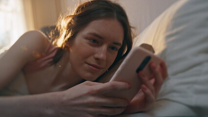 Closeup sleepy girl message smartphone in bed. Calm awake female checking mobile