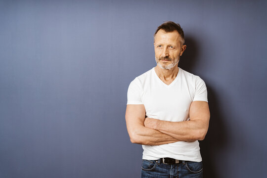 Confident Bestager Man in White T-shirt Leaning Against Blue Wall with Crossed Arms, Contemplating the Active Lifestyle Ahead with Copyspace