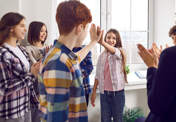 School children make friends and have fun together. Happy girl gives a high five to a boy while their friends and teacher are clapping their hands. Teamwork, friendship and support concepts