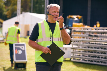 Male Production Worker With Headset Setting Up Outdoor Stage For Music Festival Or Concert