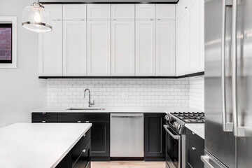 A black and white kitchen detail with a subway tile backplash, marble countertop, and large island....