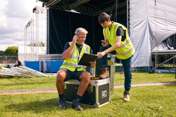 Production Team Talking On Radios And Setting Up Outdoor Stage For Music Concert Or Festival - obrazy, fototapety, plakaty