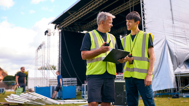 Male Production Team With Flight Cases Setting Up Outdoor Stage For Music Festival