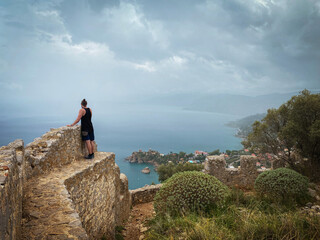 Man standing high up on an ancient stone wall enjoying the incredible view from La Rocca di Cefalù, Sicily, Italy.