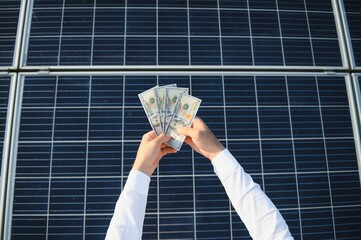 male hand hold hundred dollar at the background of solar station. concept of generation