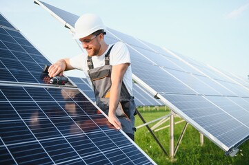 Side view of male worker installing solar modules and support structures of photovoltaic solar...