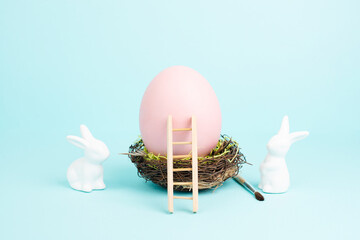 Easter bunny or rabbit sitting next to a huge pink colored egg in a birds nest, paint brush and...