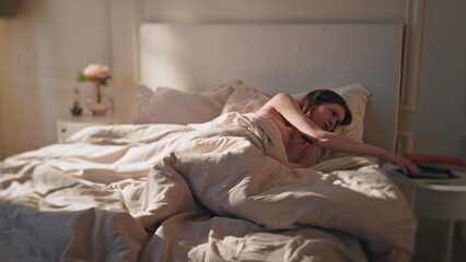 Sick woman lying home in bed morning. Tired awake female checking mobile phone