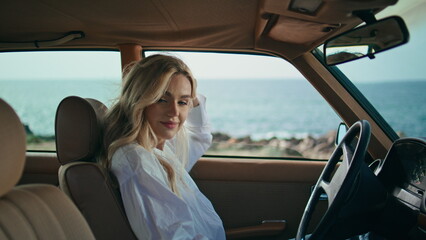 Cute blonde sitting automobile holding smartphone close up. Girl looking camera.