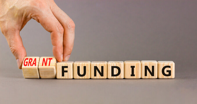 Grant funding symbol. Concept words Grant funding on beautiful wooden blocks. Beautiful grey table grey background. Businessman hand. Business and grant funding concept. Copy space.