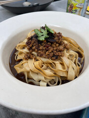 Dry Pan Mee: Malaysian dish featuring flat flour noodles served without broth, accompanied by minced meat, crispy anchovies, mushrooms, and a spicy chili paste