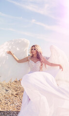 Fototapeta na wymiar beautiful girl with angel wings is walking along the seashore