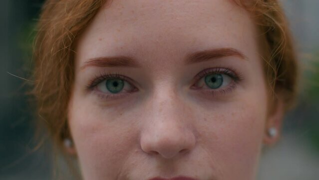 Close up beautiful smiling young Caucasian ginger woman face female lady girl slowly wide opening bright blue eyes looking camera outside city urban street. Clear vision makeup eyesight ophthalmology