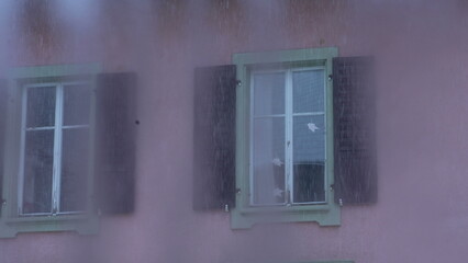 Exterior of home window during snowy day, establishing shot of residence facade while snow falls