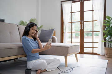 Young asian woman with headphones relaxing at home. listening to music.  sitting on cozy sofa wearing headphone