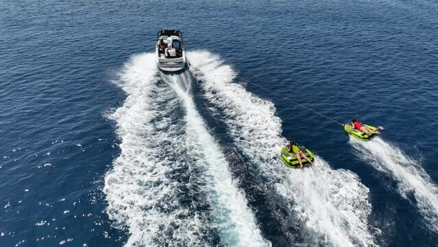 Aerial drone video of extreme inflatable towable tube cruising in high speed attached on powerboat with children on sofa ride, water sports in tropical exotic bay with deep blue crystal clear sea