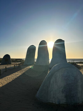 A photo captures La Mano sculpture at Punta del Este, sunlight streaming through the fingers, creating striking shadows and highlighting the iconic artwork's details against the backdrop.