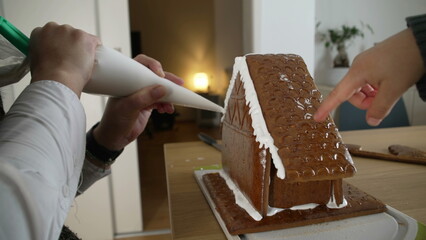 Macro close-up of person decorating gingerbread house, applying royal ice on top of sweet homemade...