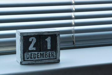 Morning December 21 on wooden calendar standing on window with blinds.