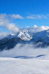 Fototapeta na wymiar Mountain covered with snow and fog. Alpine landscape in Italy, Europe. Snow-capped mountains against blue sky