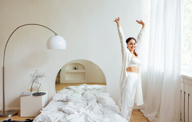 Charming young woman in white clothes and headphones woke up and stretched in her bedroom.