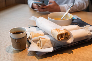 A tray with delicious shawarma, black coffee and soup on a table in a cafe.