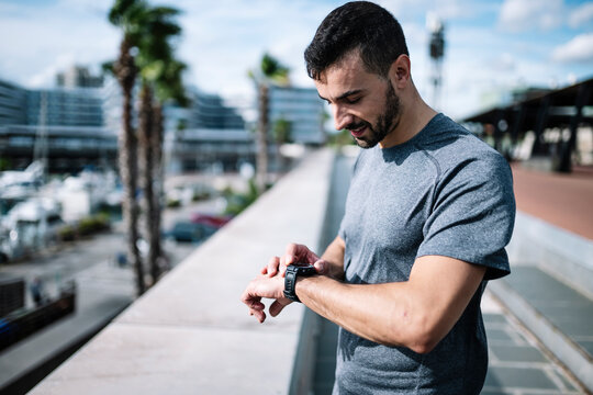 Active man looking swatch during exercise outside. Fitness male looking his smartwatch checking running time after cardio training.