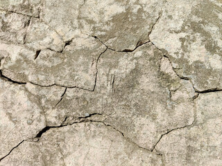 The stone wall of an old building with crumbling plaster and many winding, deep cracks. Copy space. Selective focus.