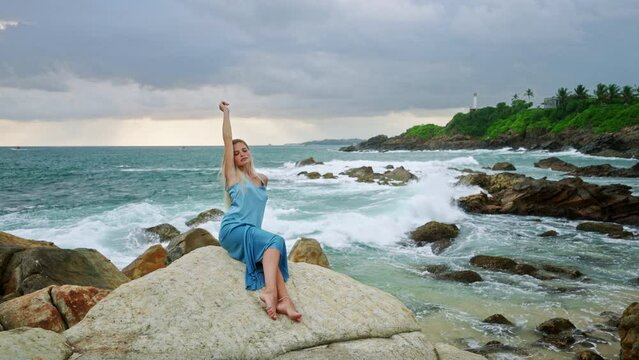 Woman meditates on cliff, sits on rocky beach overlooking sea, finds tranquility. Mental wellness with sea waves. Female combats depression in serene atmosphere , stress relief, connection with nature