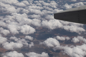 Landscape trough airplane window with clouds and part of an airplane wing