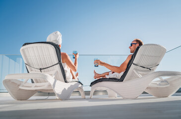 Middle-aged couple lying on the san beds on the luxury apartment terrace. They are wrapped in white...