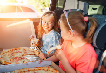 Portrait of two positive smiling sisters eating just cooked italian pizza sitting in child car...
