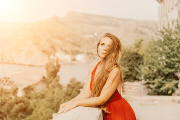 Woman red dress. Summer lifestyle of a happy woman posing near a fence with balusters over the sea.