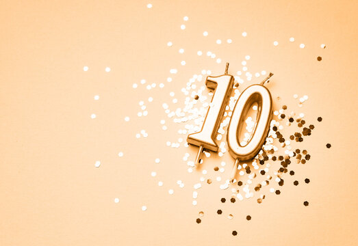 10 years celebration festive background made with golden candles in the form of number Ten lying on sparkles. Universal holiday banner with copy space.