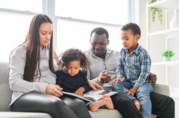 family with boy and girl child posing on photo shooting, sitting on couch and reading book