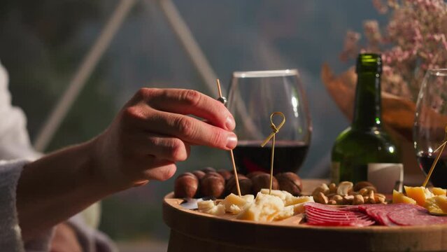 Male hand impales cheddar onto skewer closeup. Man enjoys assortment of delicious snacks at wine table in restaurant. Appetizers plate for romantic dinner
