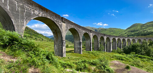 Fototapeta na wymiar Glenfinnan viaduct bridge in green highlands landscape in summer, travel Scotland