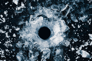 The round hole in the ice on a black background. Shards of crushed ice spread away.