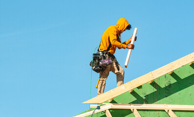 Front view of, a contractor securing house roof trusses, against blue sky
