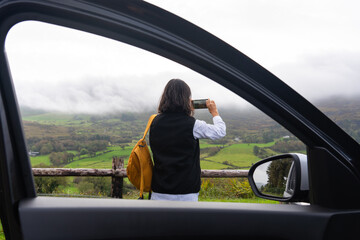 Unrecognizable woman with backpack stopping her rental car next to the road taking a photo of a...
