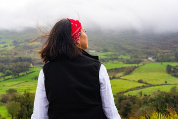 Latin woman enjoying the silence and peace of a beautiful Irish landscape on a stop on her road...